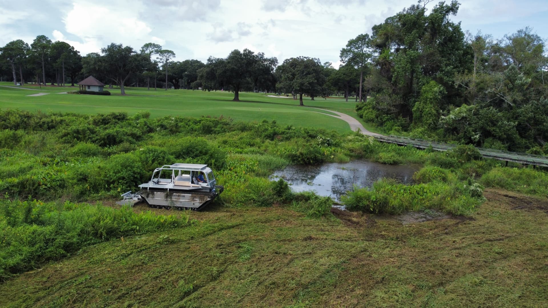 SKS Aquatic amphibious mower clearing vegetation from a golf course wetland